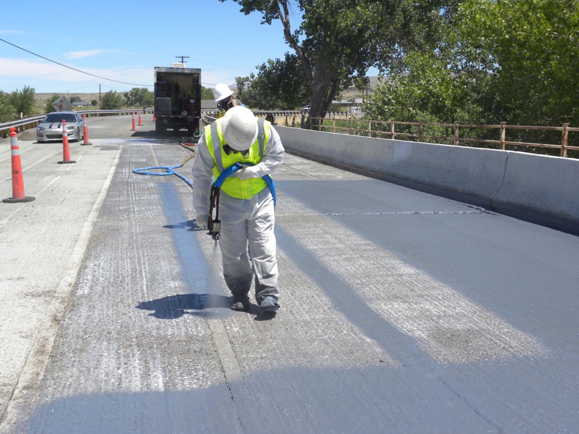 worker wearing a green vest and gray suit spraying a road